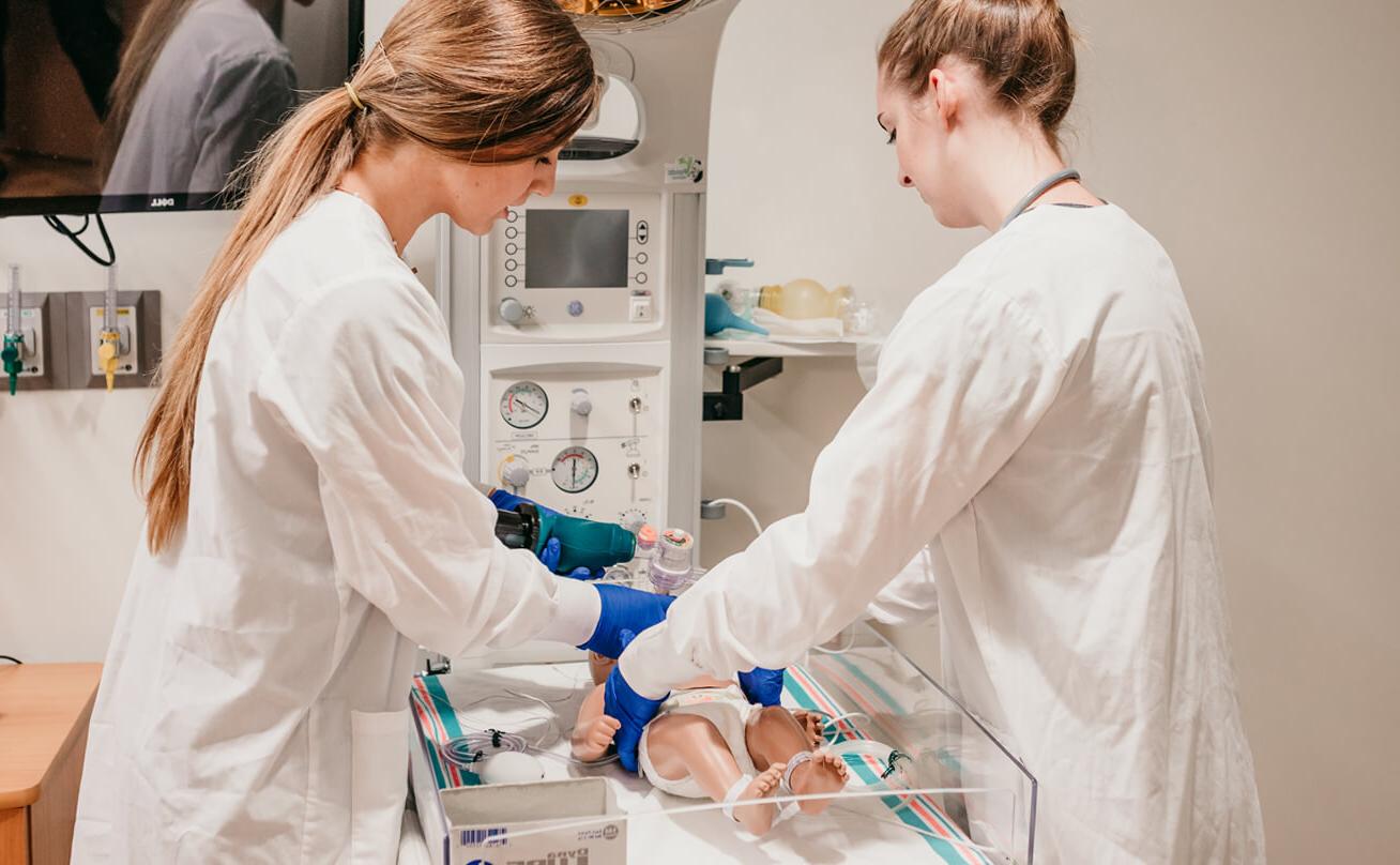 Student assists another student with baby nursing manikin
